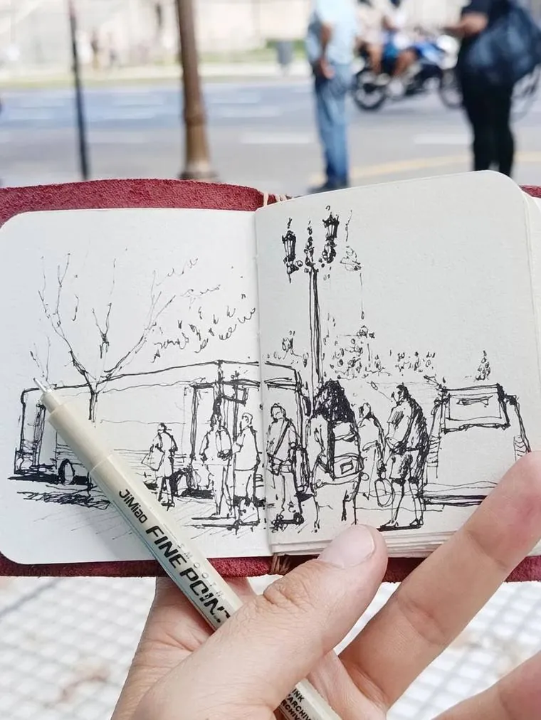 Bitácora de bolsillo abierta en la calle, con un dibujo en tinta de una parada y un rotulador apoyado