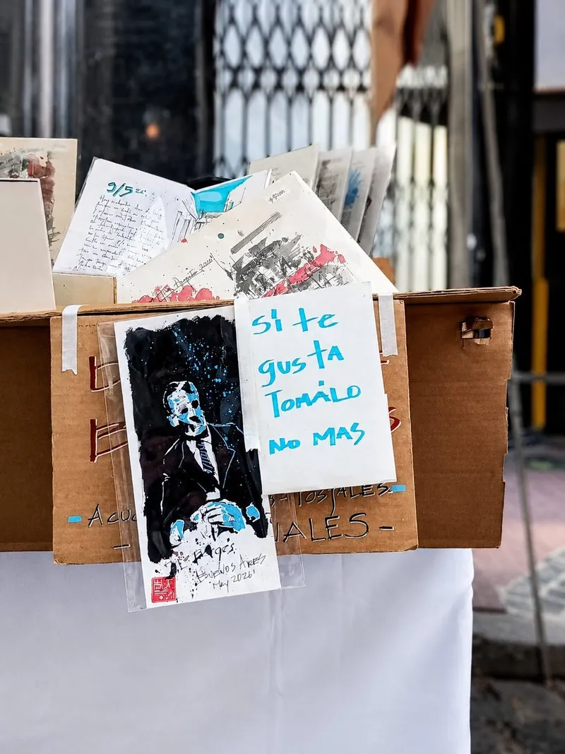 Ilustración en tinta y azul sobre papel, expuesta en un puesto de la calle con el cartel "Si te gusta, tómalo no más"