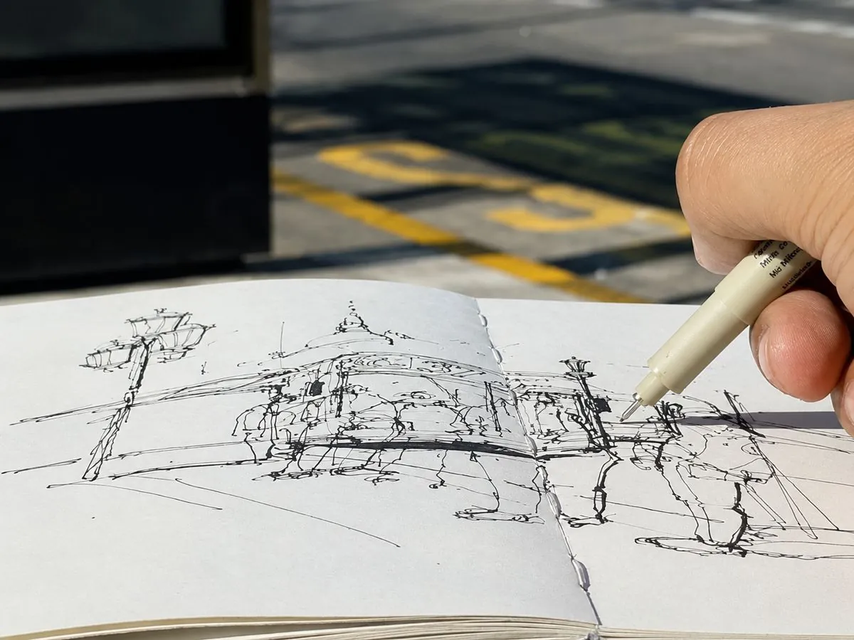 Mano entintando un dibujo en un cuaderno, con la parada de colectivo de Congreso al fondo