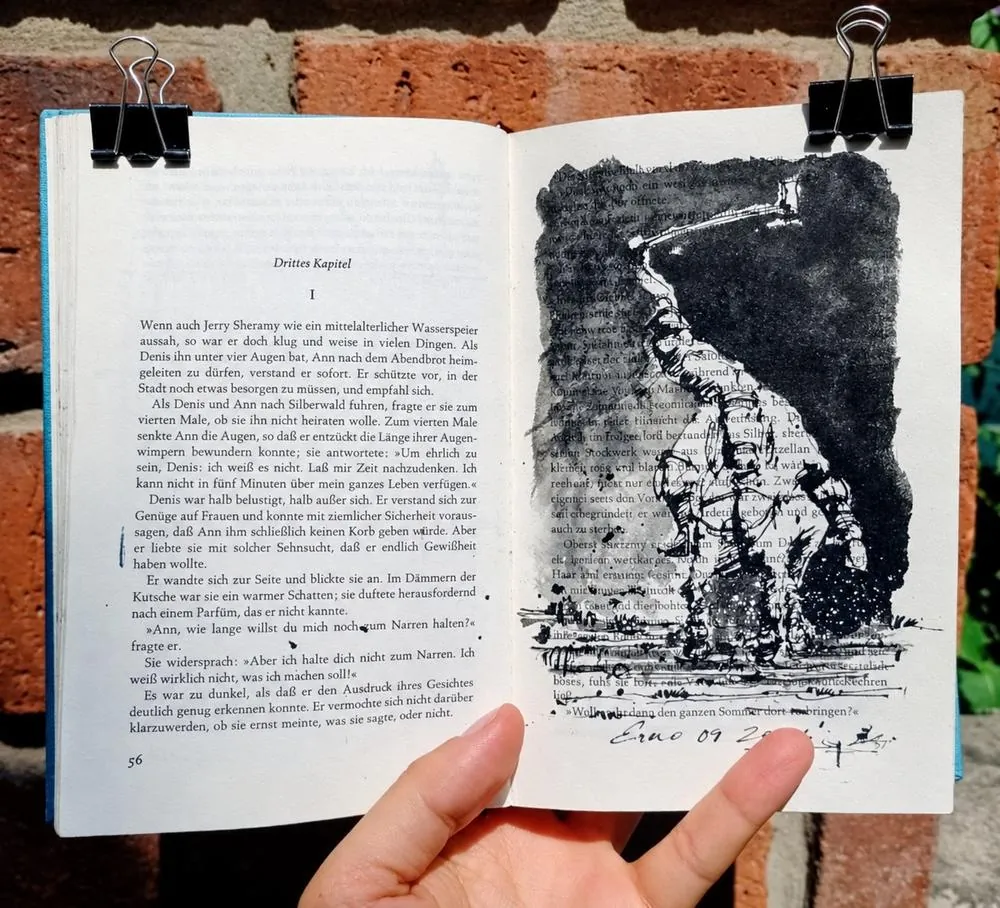 Novela en alemán abierta y sujeta con pinzas contra una pared de ladrillo, con una figura en tinta china negra sobre la página impresa