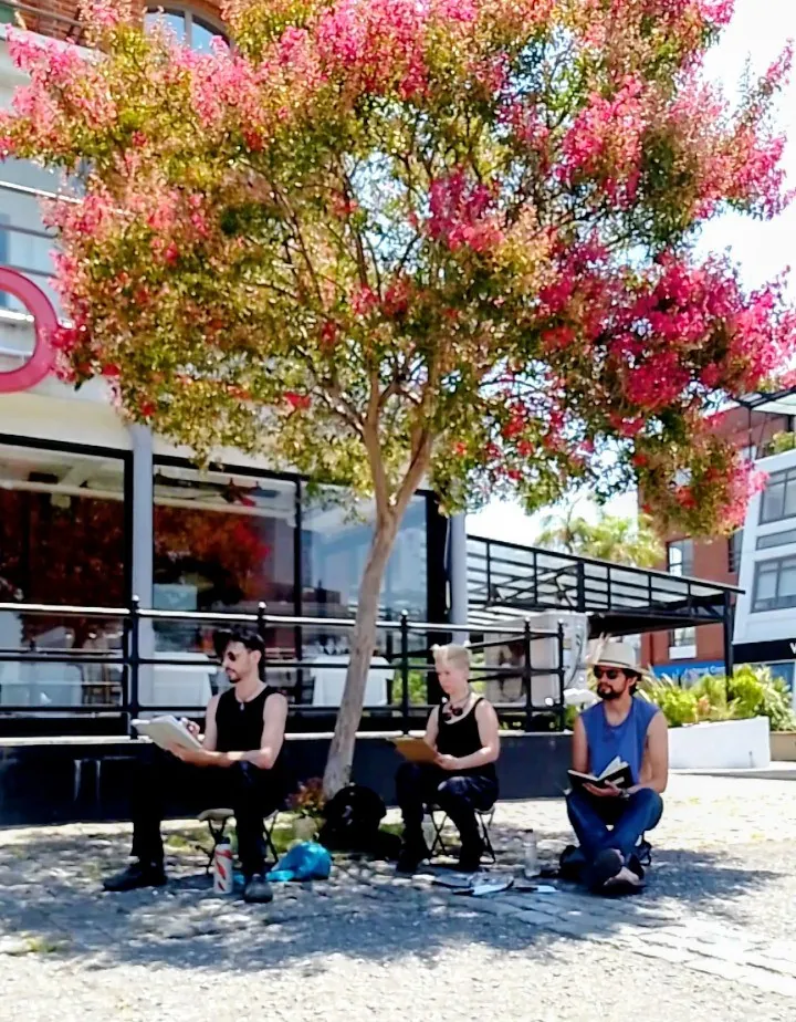Tres personas dibujando sentadas bajo un árbol florido